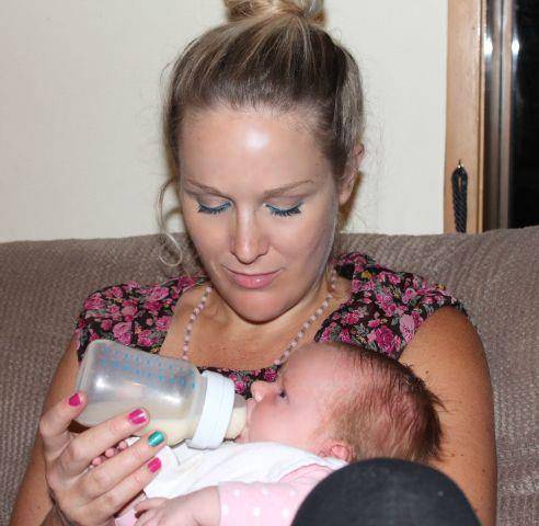 Mother with bun in hair, holding brand new baby while feeding them a bottle of milk