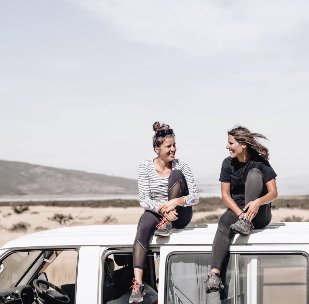 Two happy young ladies laughing and having fun, sitting on top of the van while traveling. These two ladies love adventure, road trips and become wild to pursue happiness
