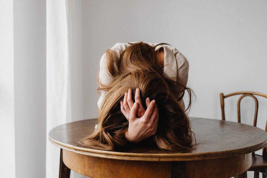 Frustrated woman resting her head on an old oak table while cradling her head in her hands