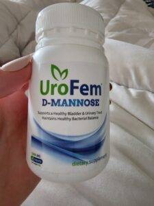 A woman's hand holding a bottle of Urofem, a D-Mannose supplement for urinary tract health.